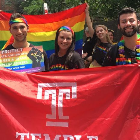 Students and alumni carrying a rainbow Pride flag and a Temple Flag.