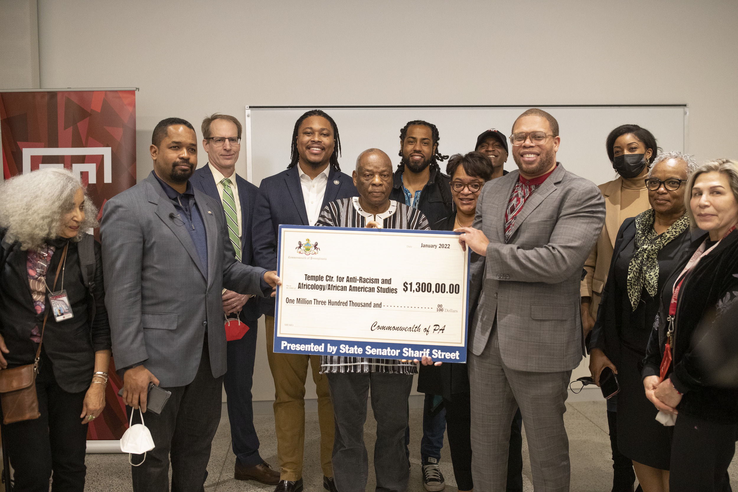 A group of 12 people pose for a picture while holding a large novelty check.