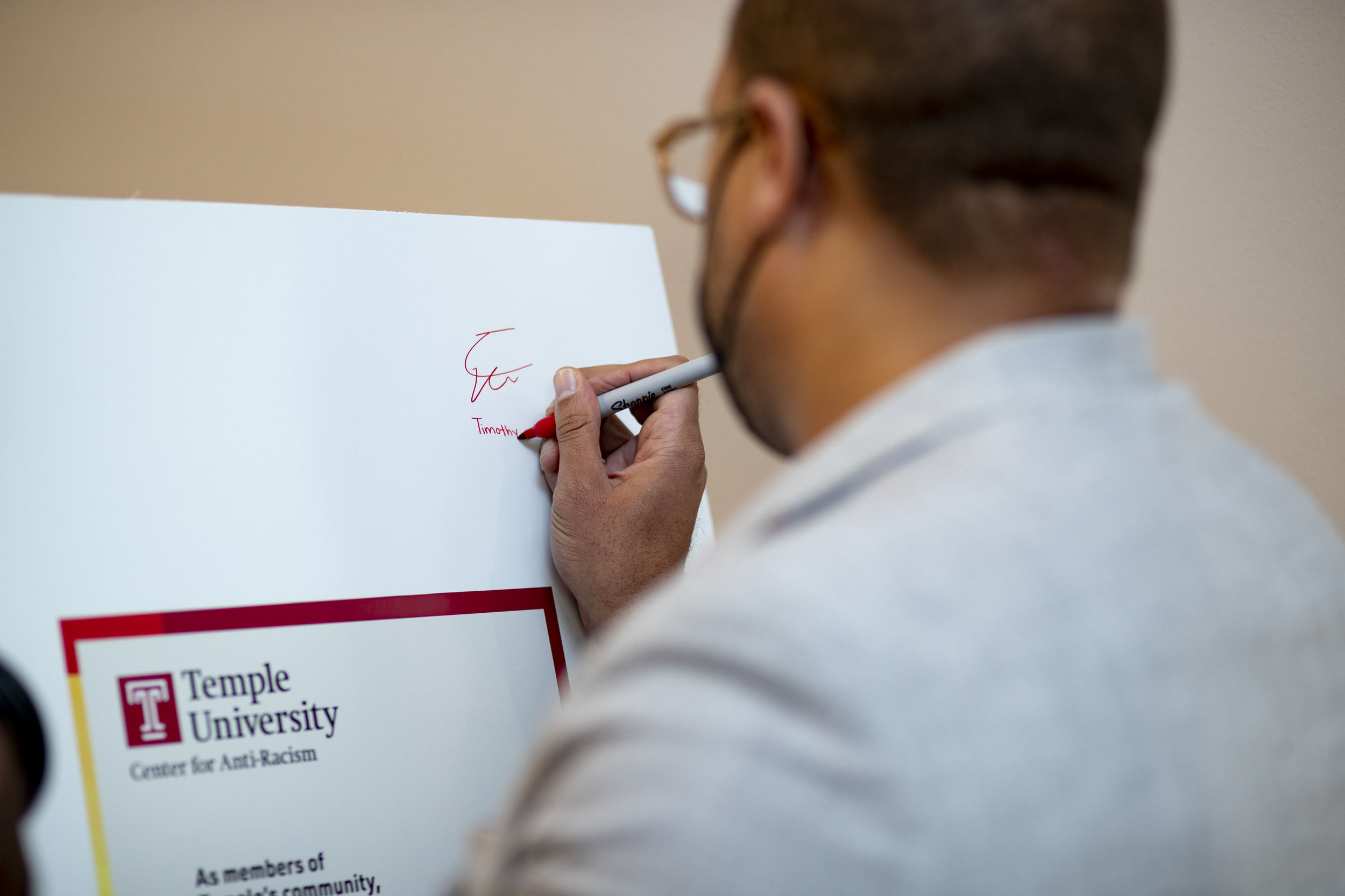 The back of a man's head is shown while he signs a poster board.