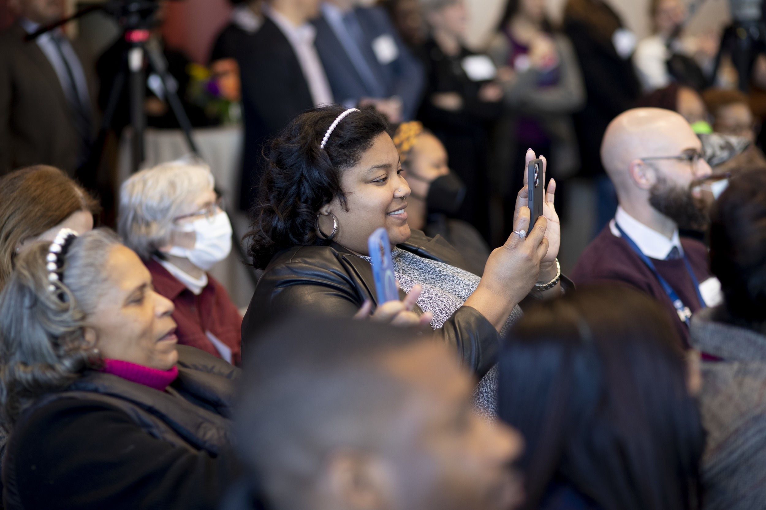 People in the audience are smiling and taking pictures with their phones.