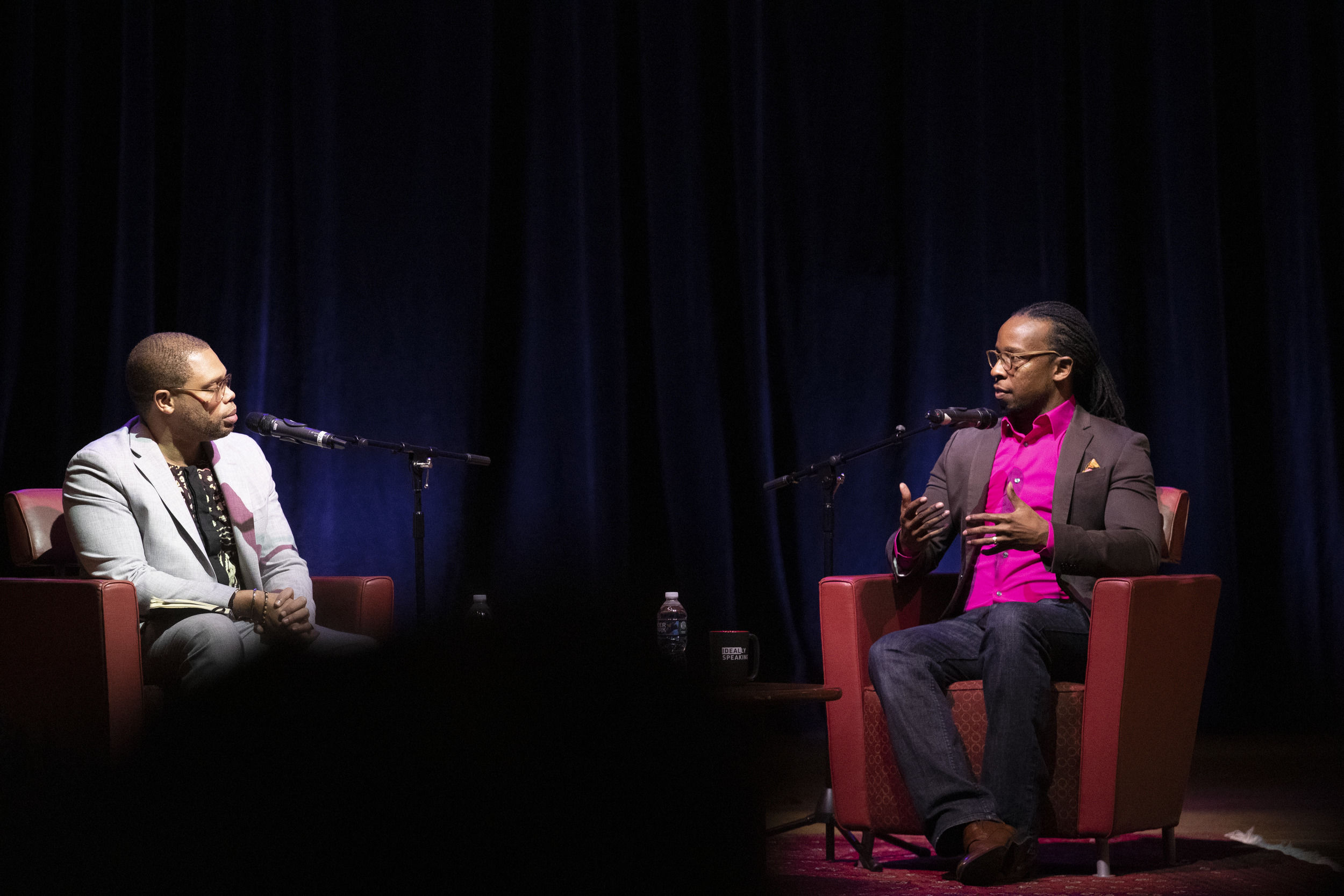 Two men face each other while sitting on chairs.