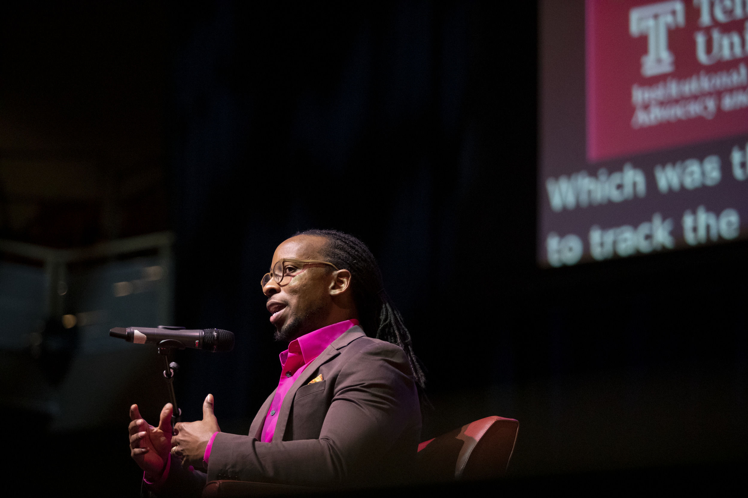 A man with a pink shirt is shown speaking into a microphone.