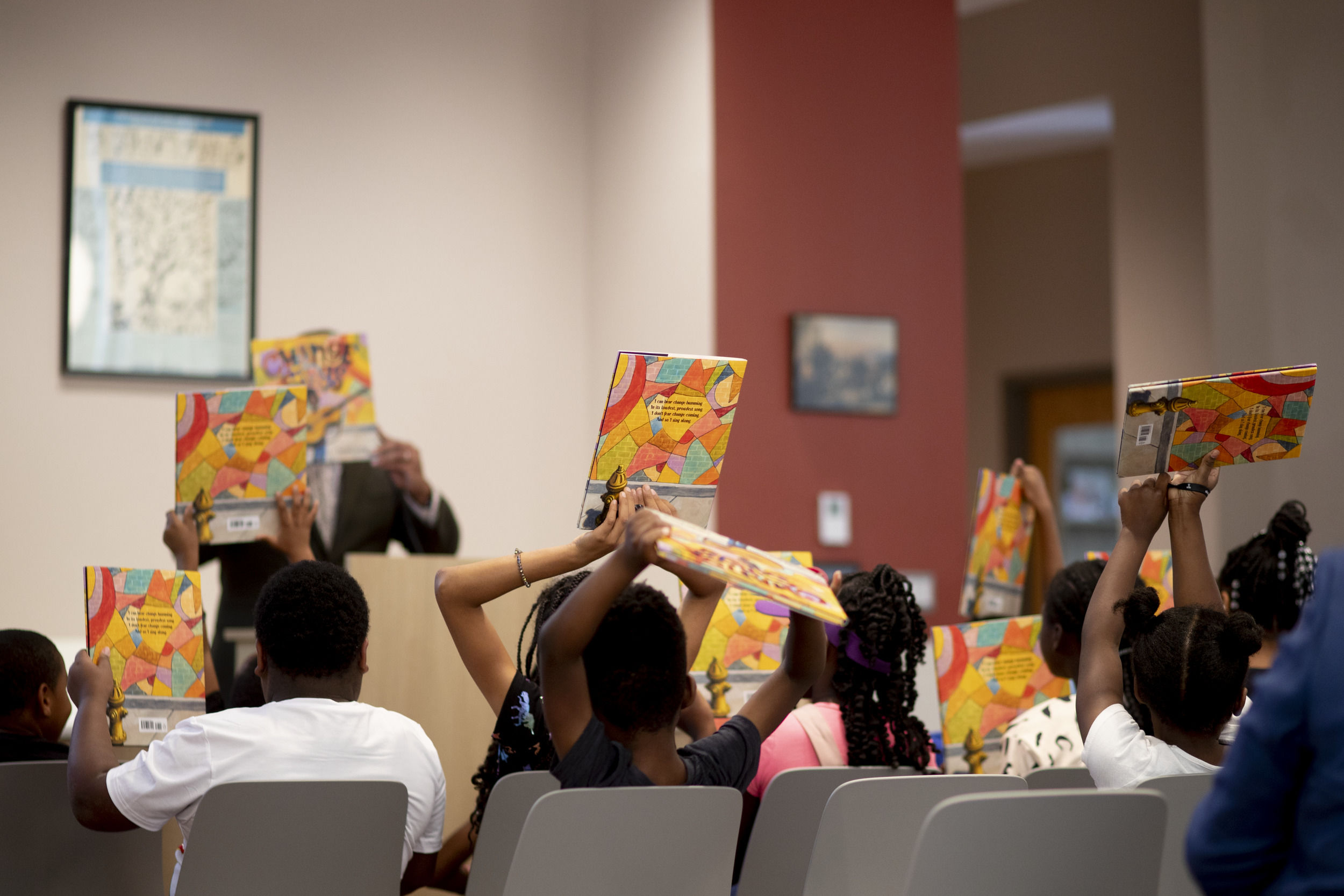 A group of children hold up a book in their hands while sitting in chairs. 