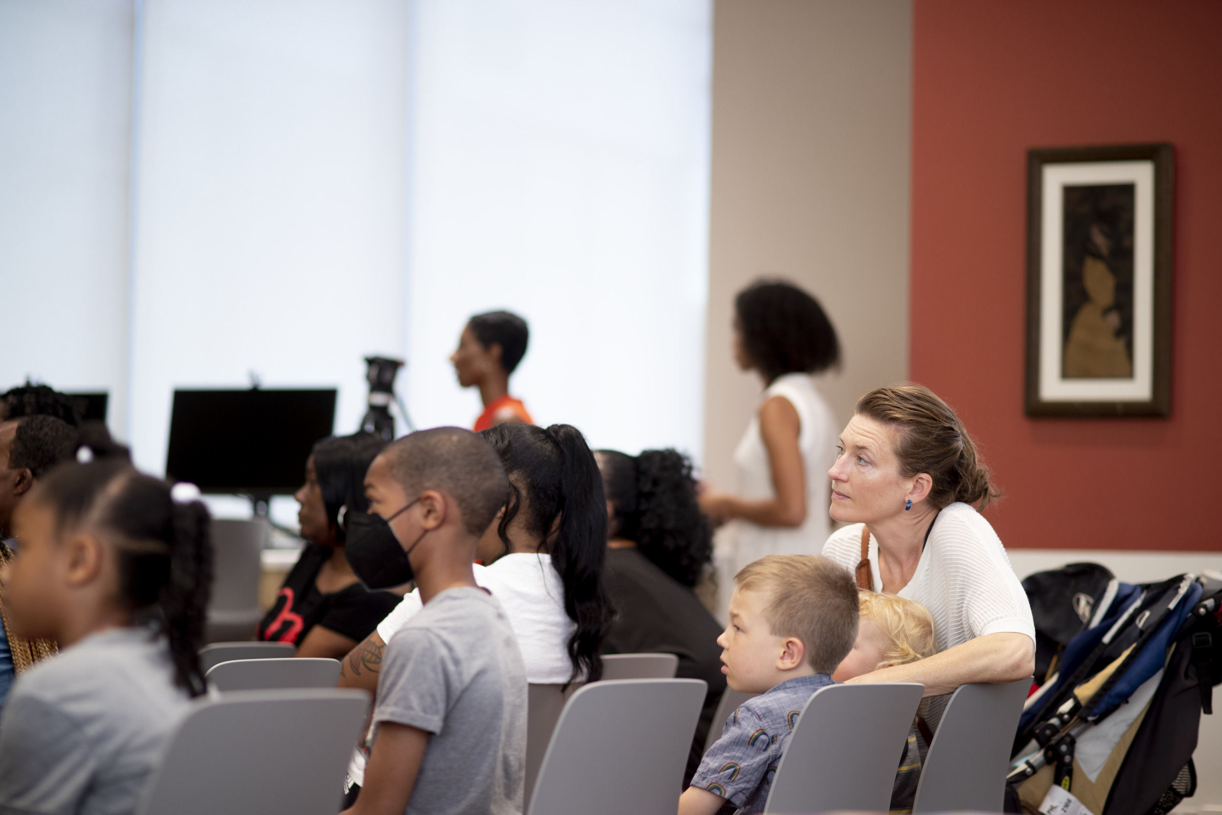 Adults and children sit in chairs while looking forward.