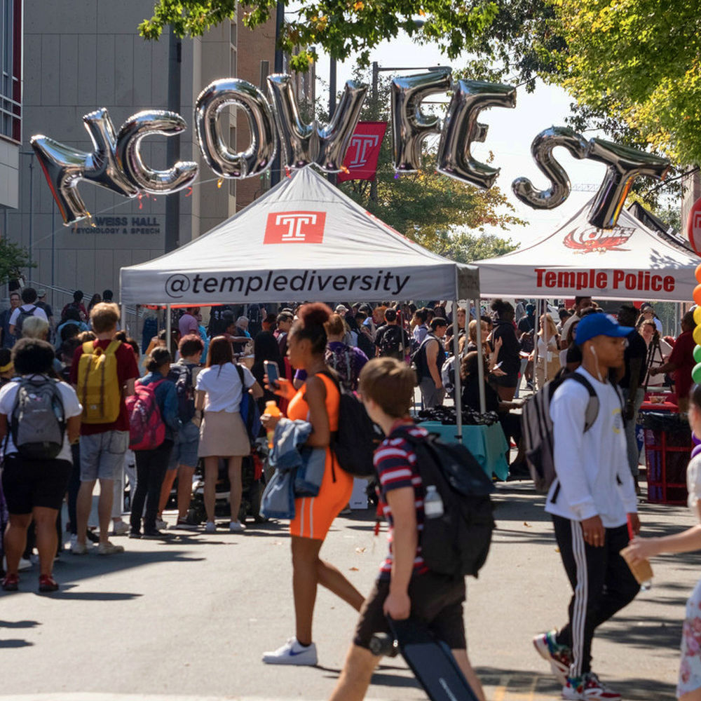 The ncow festival with people walking in various directions. There are arching balloons that spell out the words NCOWFEST above the institutional diversity tent